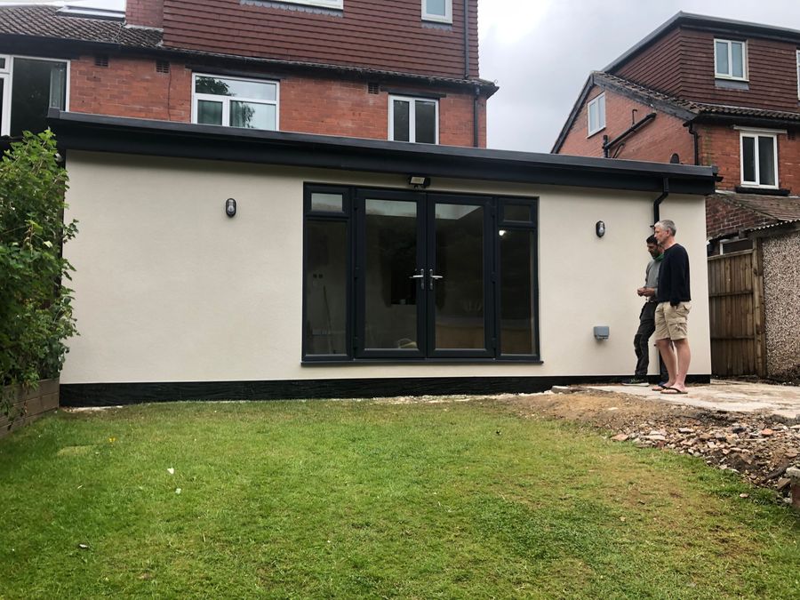 White rendered rear extension with dark glazing, homeowners looking on