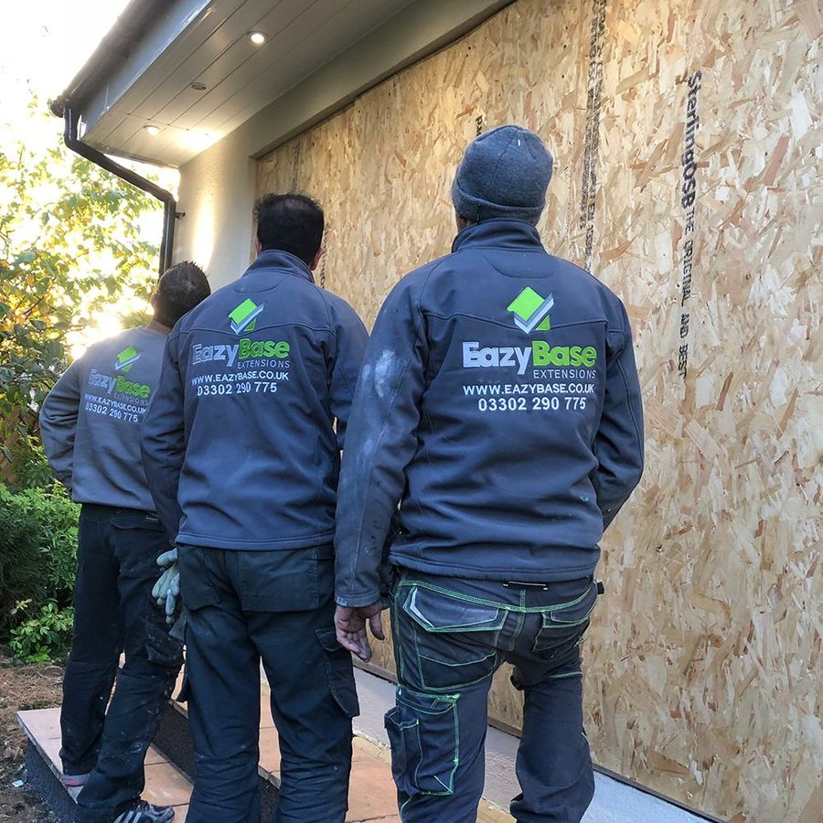 Two EazyBase team members in branded jackets reviewing an extension build on site